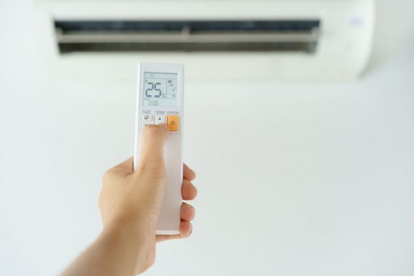 Close-up of woman hand operating air conditioner with remote control. Open air conditioning 25 degrees.